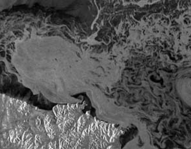 This 1998 RADARSAT-1 image reveals grease ice along a pack-ice front in the Bering Sea. Grease ice forms after frazil (slush-like ice) crystals are pushed against each other. When the fragile "arms" of the crystals break and form a mixture of damaged crystals and crystal remnants, the result is grease ice—an oily-looking "ice soup" on the water surface. Its viscous nature smooths out small ocean waves. © CSA, 1998.