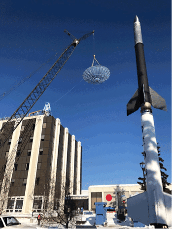 A 250-foot crane lifts the original antenna off the top of the Elvey Building, framed by an outdoor rocket display, part of the Geophysical Institute.